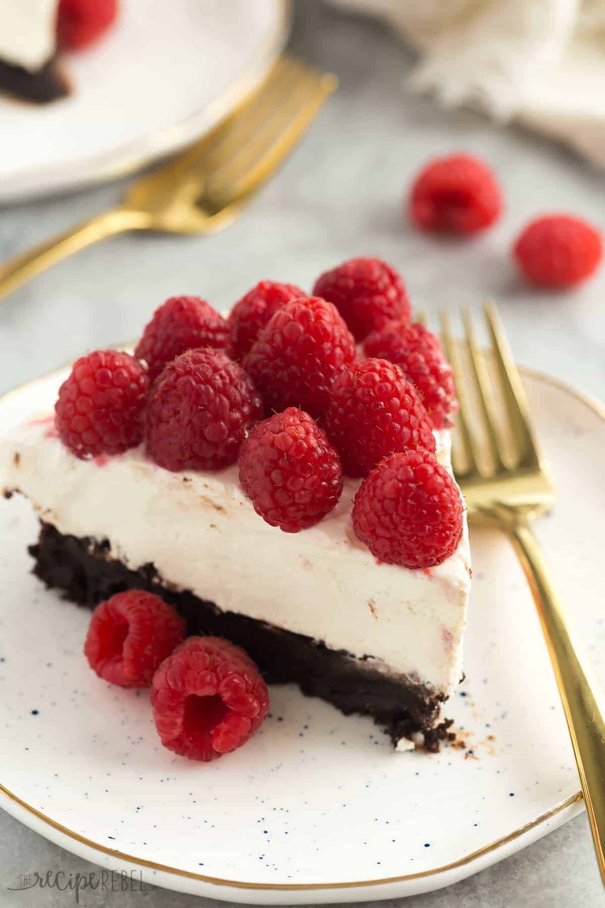 brownie bottom cheesecake slice on white speckled plate with gold fork on the side