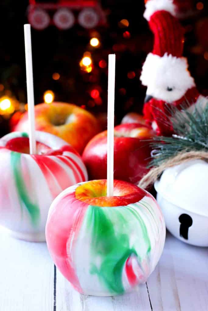 weihnachtlich marmorierte getauchte Äpfel mit weißen Stangen und weihnachtlicher Dekoration im Hintergrund