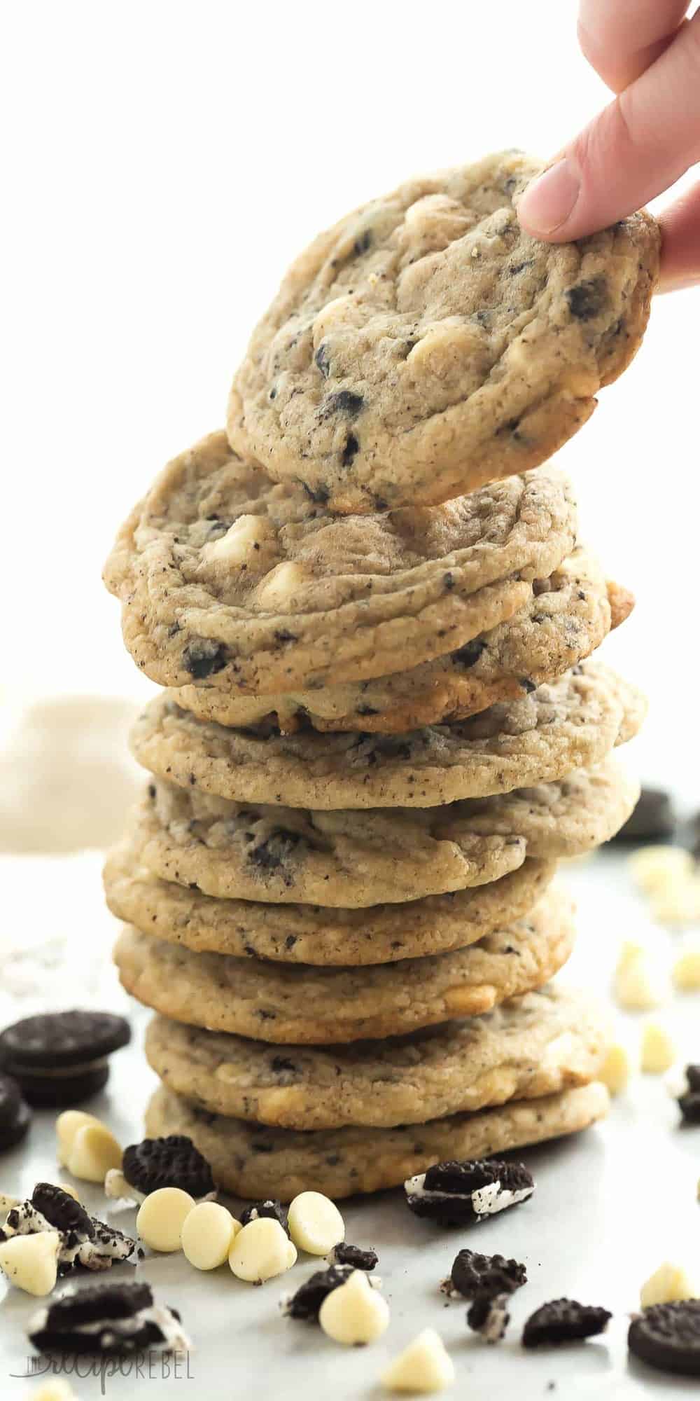 tall stack of cookies and cream cookies with white chocolate chips and crushed oreos on a white background