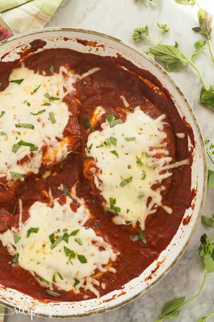 This Skillet Chicken Parmesan is made healthier with a homemade tomato sauce, skinless chicken breasts and no breading or frying (which means it's also gluten free)! It's a 30 minute meal that everyone will love! overhead image of white pan with skillet chicken parmesan in tomato sauce with fresh parsley