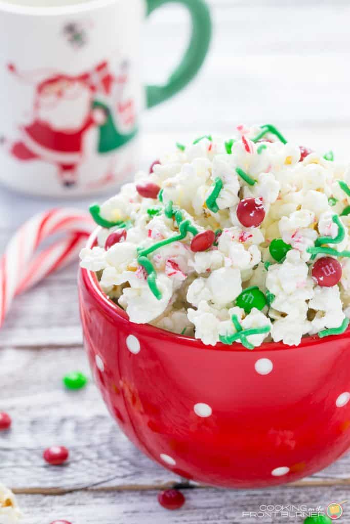 white chocolate peppermint popcorn piled high in red bowl with christmas M&Ms