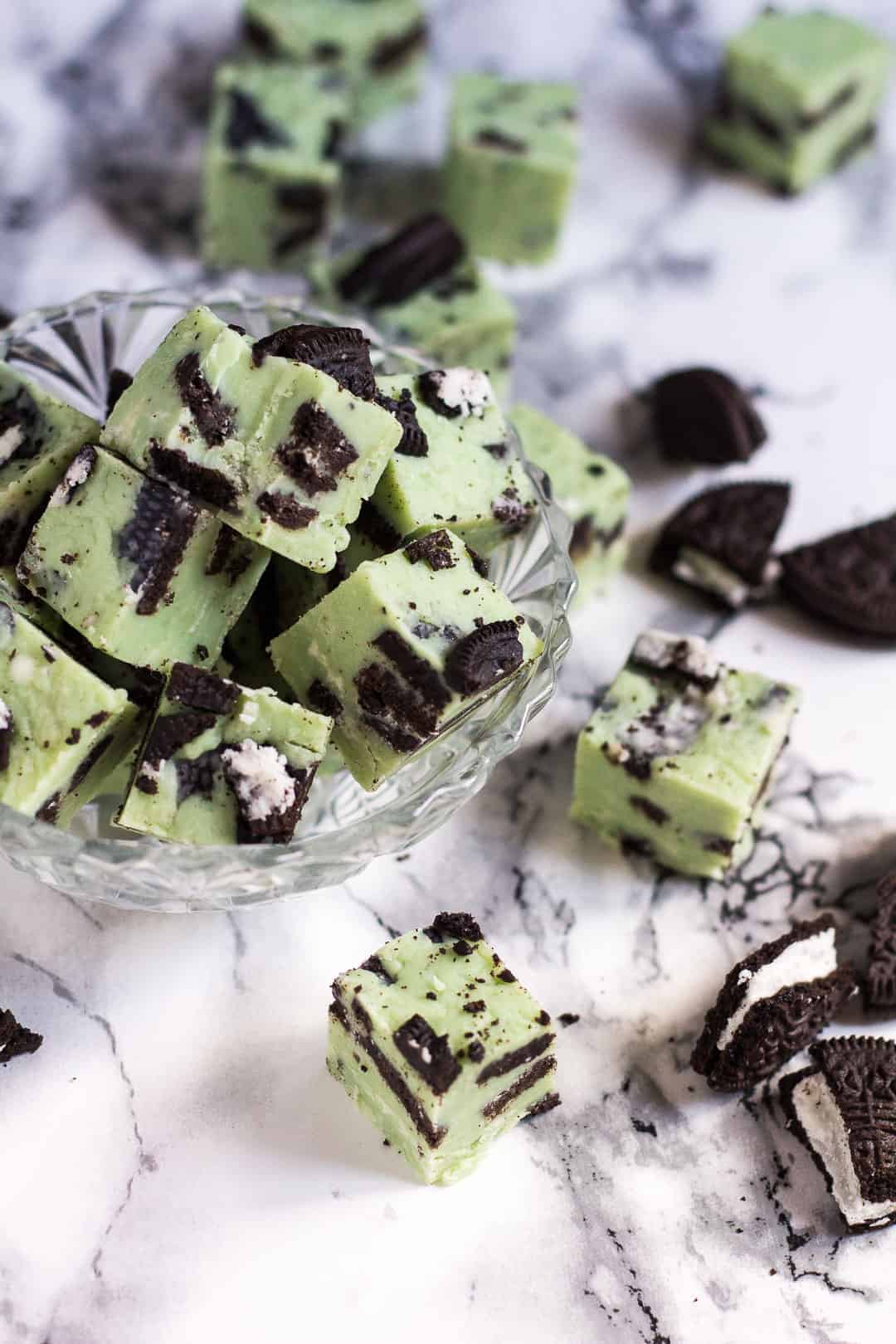 mint oreo fudge stacked in glass bowl with pieces on marble background around bowl