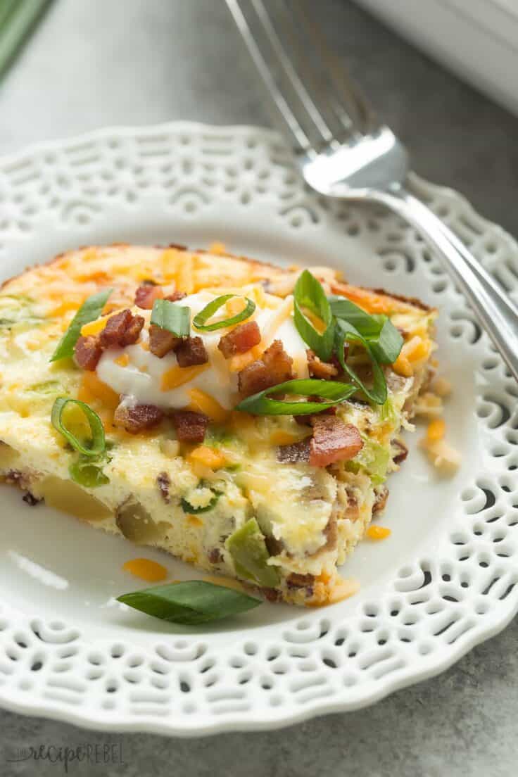 loaded baked potato breakfast casserole piece on white plate with sour cream and green onions