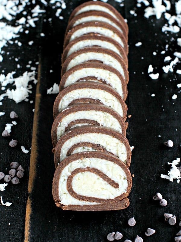 No Bake Almond Joy Roll aufgeschnitten auf schwarzem Untergrund mit Kokosnuss um die Rolle
