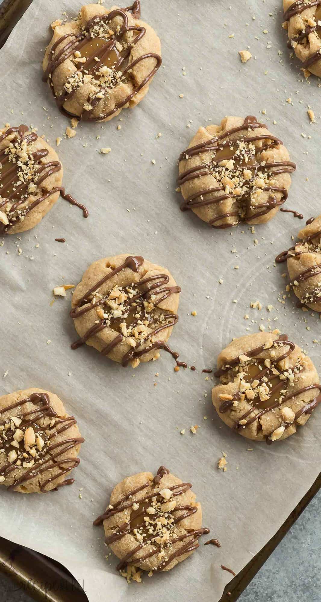 These Peanut Butter Turtle Thumbprint Cookies are a new twist on a classic Christmas cookie -- with a peanut butter cookie base, a simple caramel filling, a drizzle of chocolate and a sprinkling of peanuts, they're sure to be a new holiday tradition!