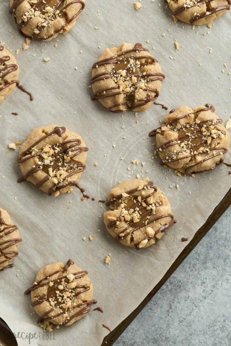 peanut butter turtle thumbprint cookies on a parchment lined sheet pan