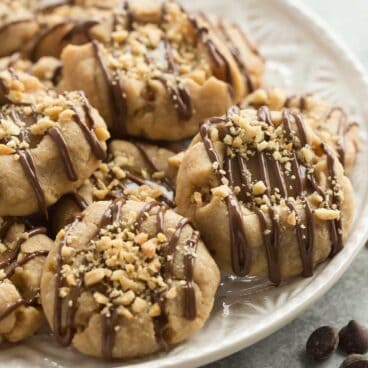 These Peanut Butter Turtle Thumbprint Cookies are a new twist on a classic Christmas cookie -- with a peanut butter cookie base, a simple caramel filling, a drizzle of chocolate and a sprinkling of peanuts, they're sure to be a new holiday tradition!