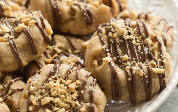 These Peanut Butter Turtle Thumbprint Cookies are a new twist on a classic Christmas cookie -- with a peanut butter cookie base, a simple caramel filling, a drizzle of chocolate and a sprinkling of peanuts, they're sure to be a new holiday tradition!