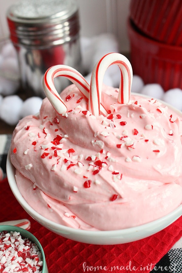 peppermint fluff dip in a white bowl with crushed candy canes on top and candy canes stuck in the top