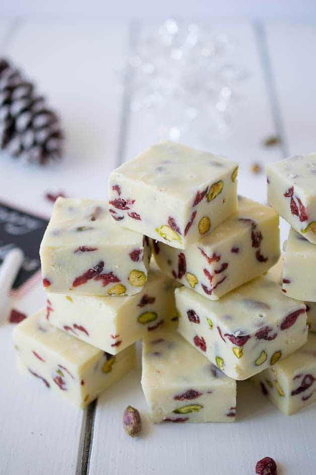 white chocolate pistachio cranberry fudge stacked on a plate with christmas decorations in the background