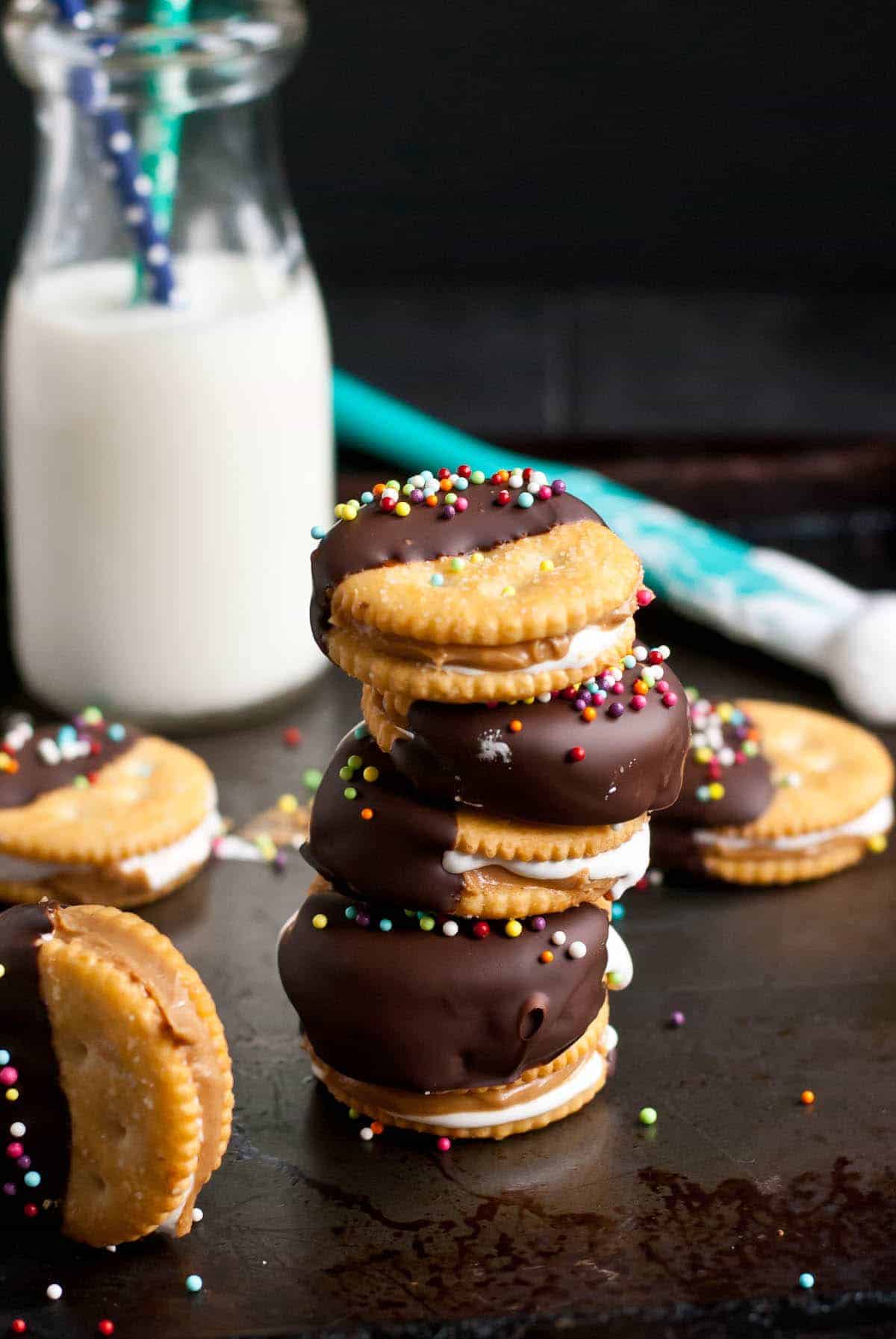 chocolate dipped fluffernutter ritz cookies stacked with a black background and glass of milk in the background