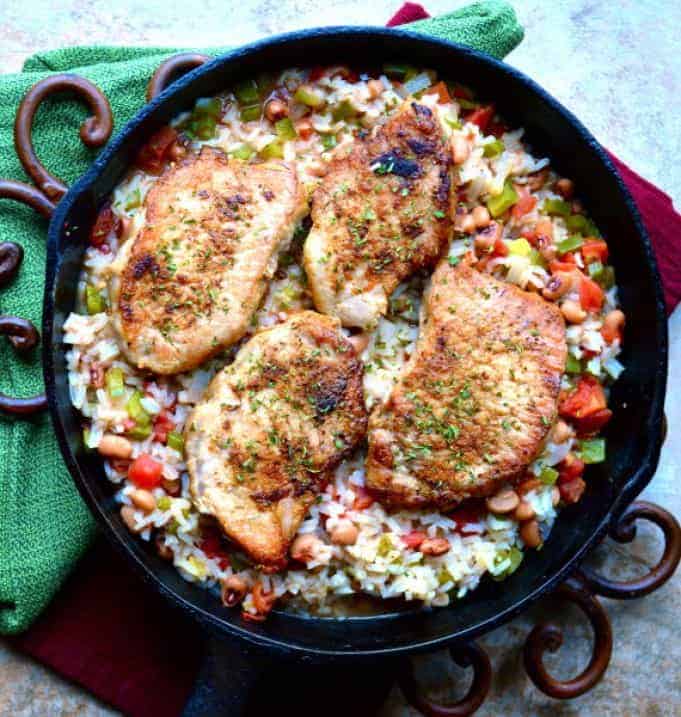 cast iron skillet with spicy pork chops on rice with vegetables and beans