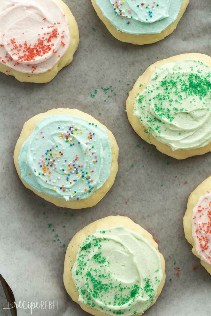 grandma's sour cream cookies with pink blue and green frosting and sprinkles on a sheet pan