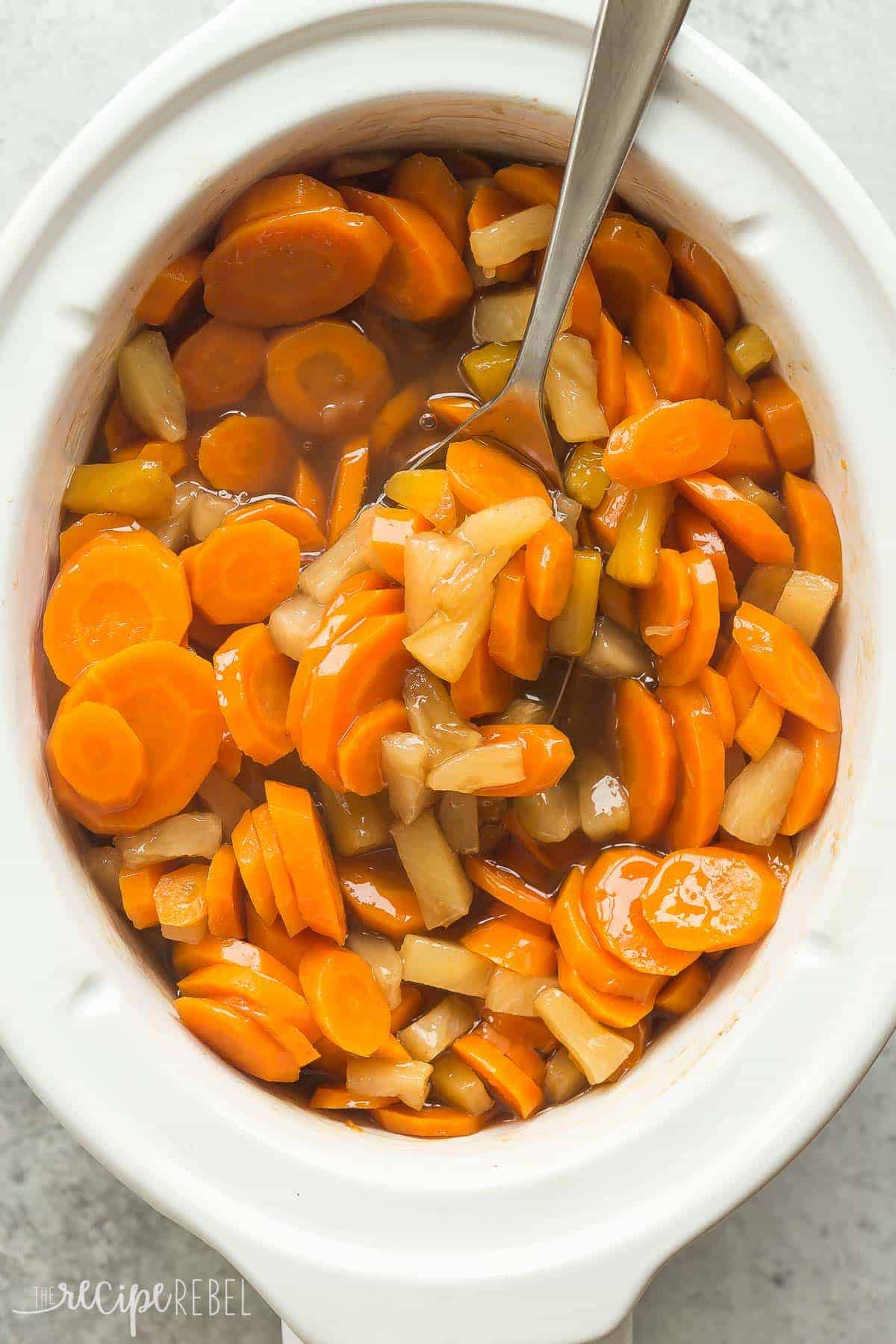 overhead image of white slow cooker with pineapple glazed carrots in metal spoon