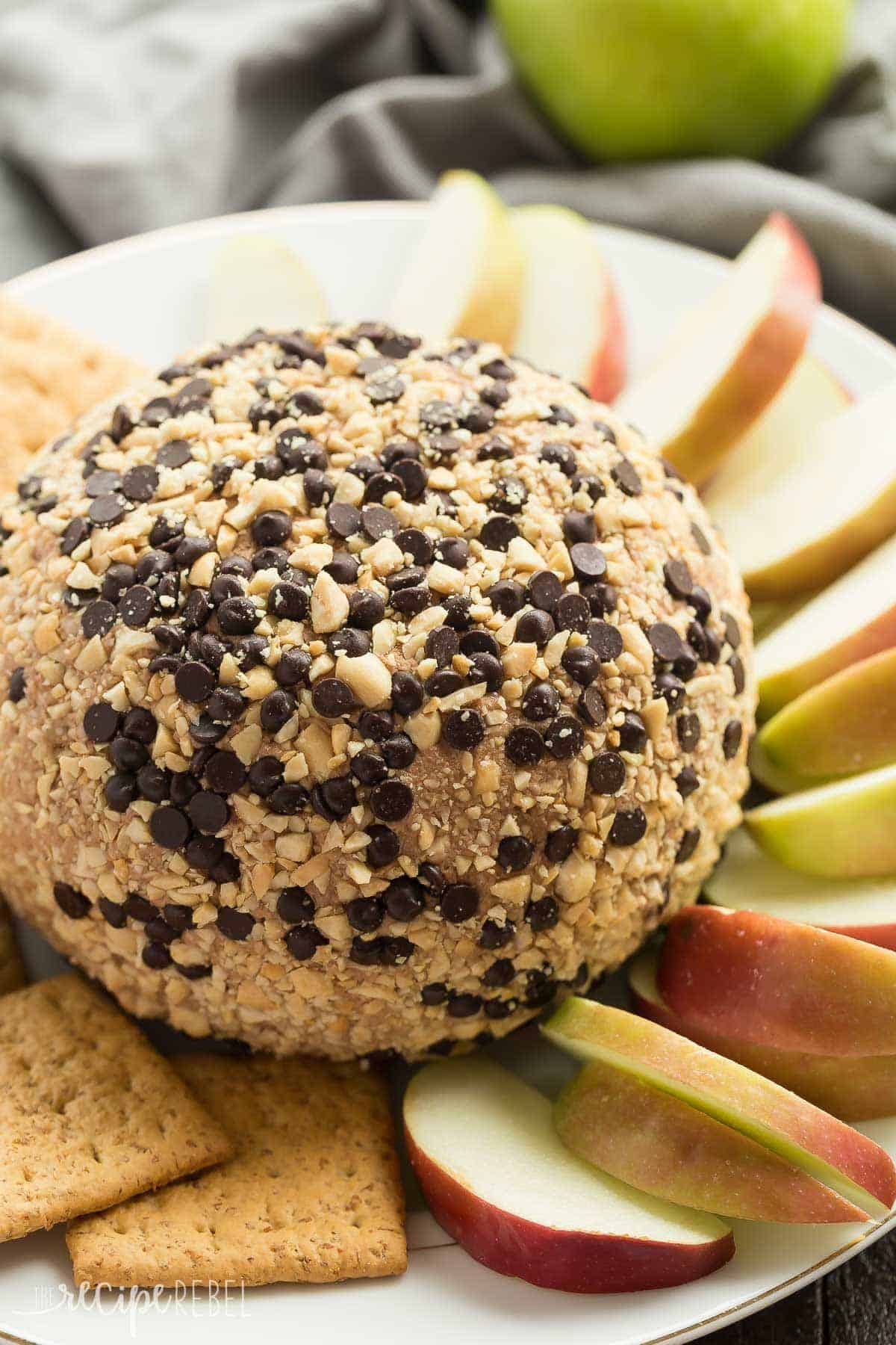 snickers cheese ball whole covered in mini chocolate chips and toffee bits with sliced apples