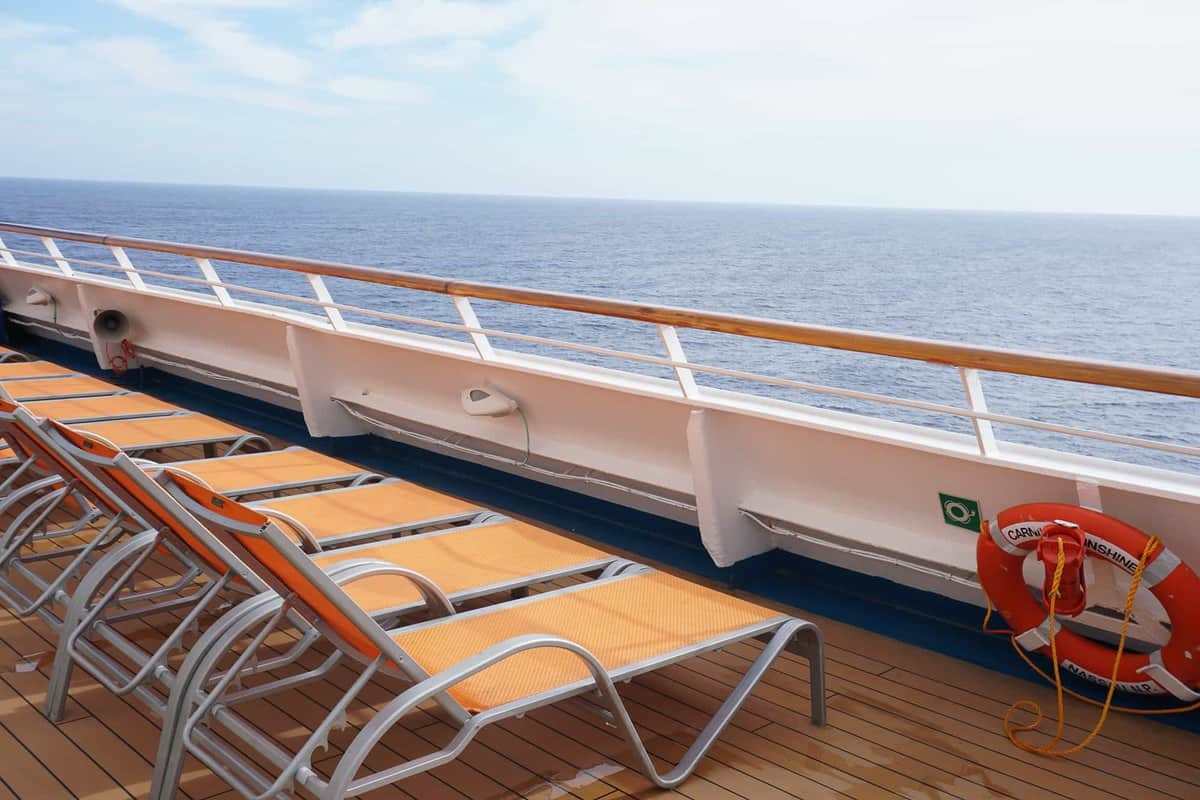 cruise ship railing with lounge chairs and looking out to the ocean