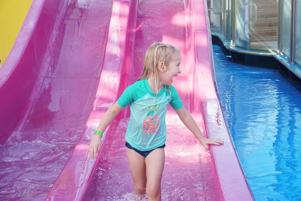 girl at the end of pink kids slide on carnival sunshine