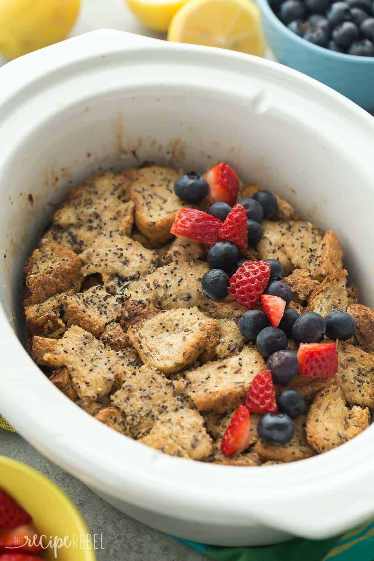 This Overnight Slow Cooker Lemon Poppy Seed French Toast is an easy, overnight breakfast or lunch! It's packed with lemon flavor and topped with fresh berries, perfect for a relaxing weekend breakfast. lemon poppy seed french toast casserole in the slow cooker with fresh strawberries and blueberries
