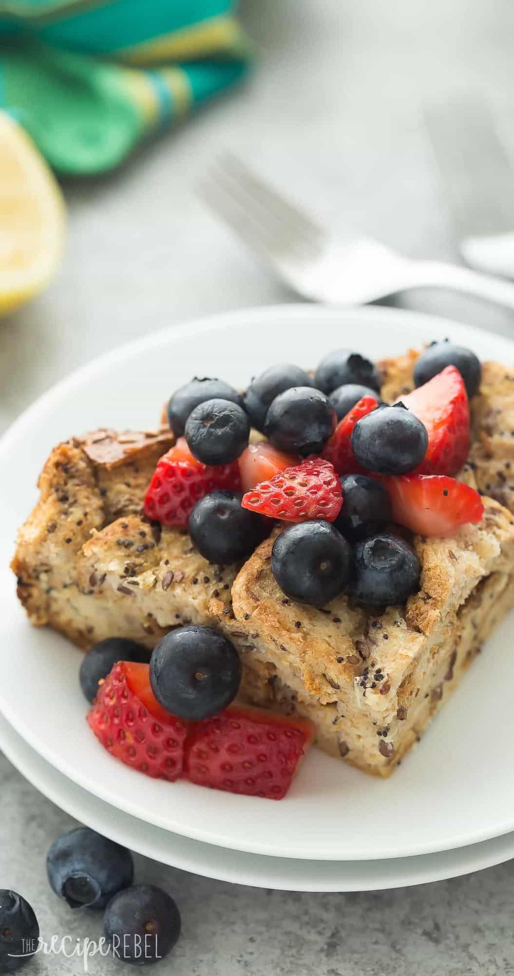 close up image of slice of french toast casserole on white plate with fresh strawberries and blueberries
