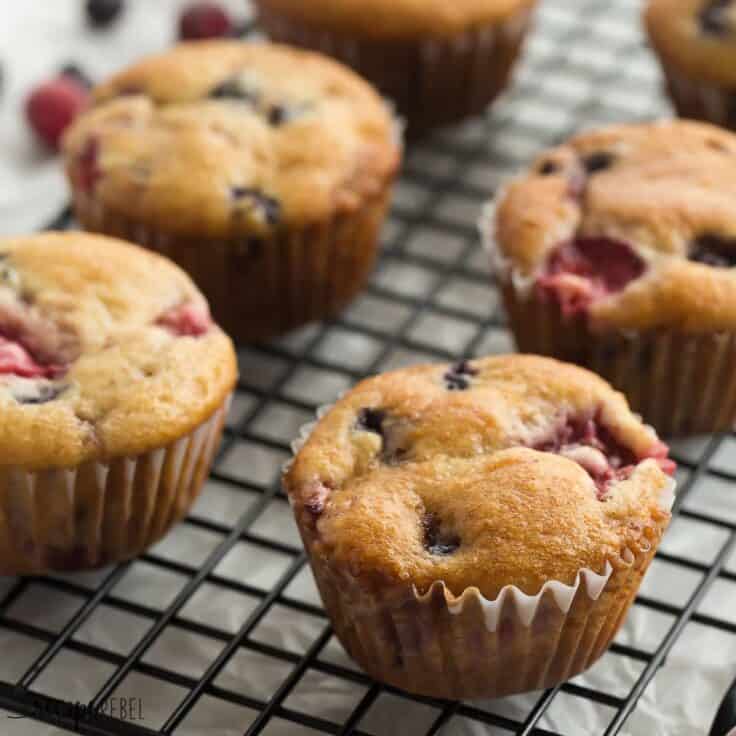 These Fruit Explosion Muffins are loaded with strawberries and blueberries (or any berries you want!) and have a strawberry jam surprise inside! They are made with whole wheat flour and sour cream makes them extra moist. Square image of fruit explosion muffins on black cooling rack.