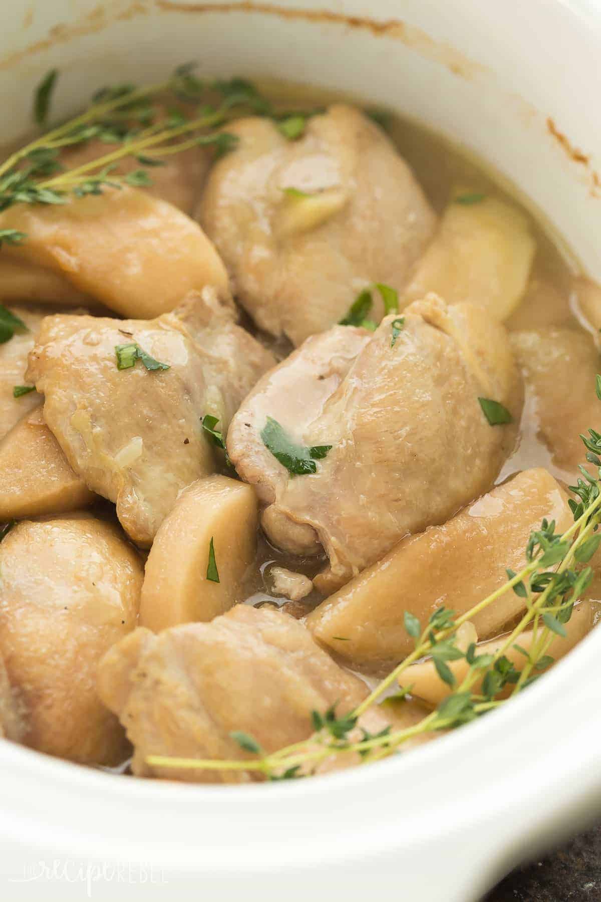 white crockpot with chicken thighs and apples and thyme sprigs