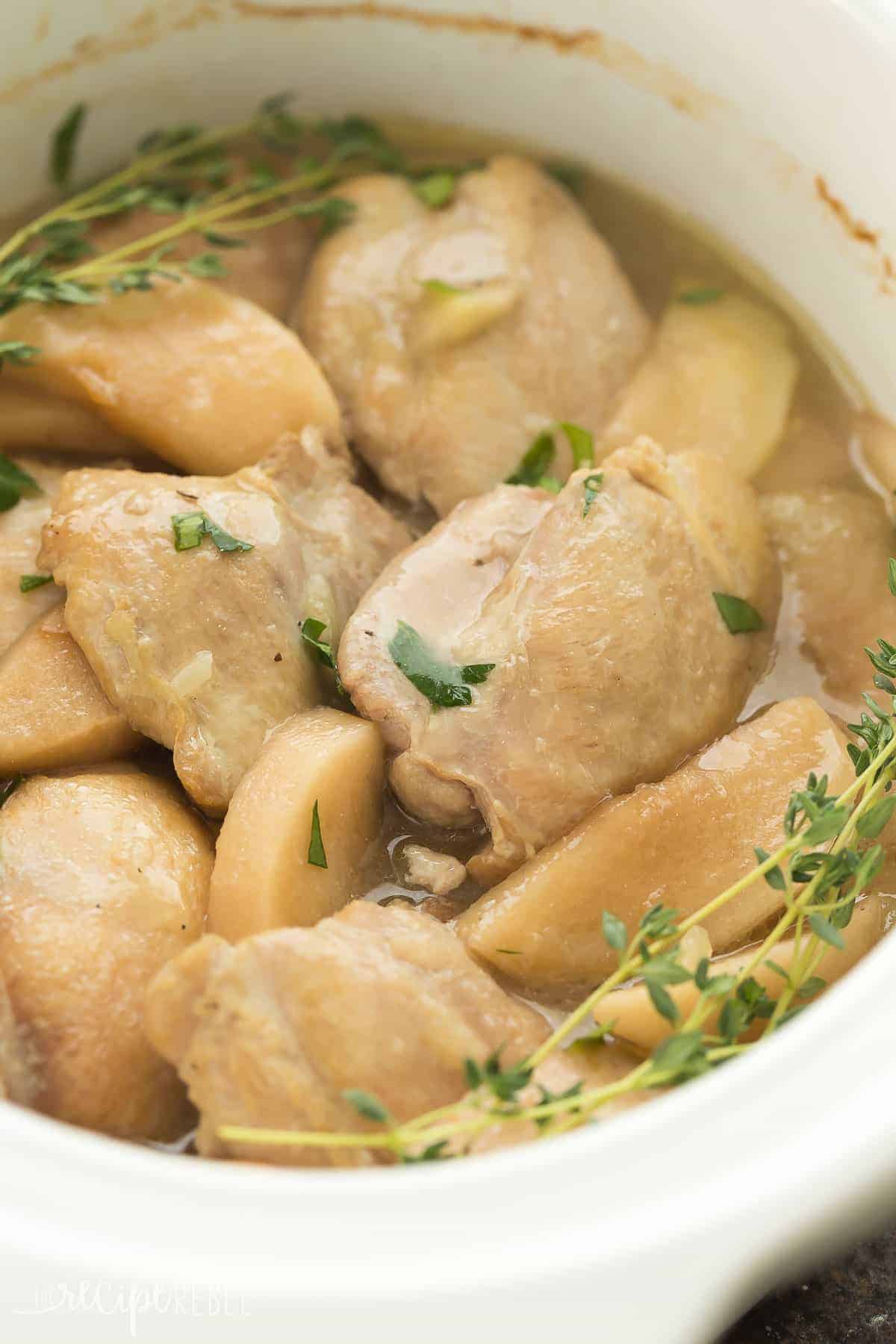 These Slow Cooker Chicken Thighs with Apples are the perfect mix of sweet and savory -- an easy but elegant dinner recipe for Sunday dinner or a busy weeknight! white crockpot with chicken thighs and apples and thyme sprigs