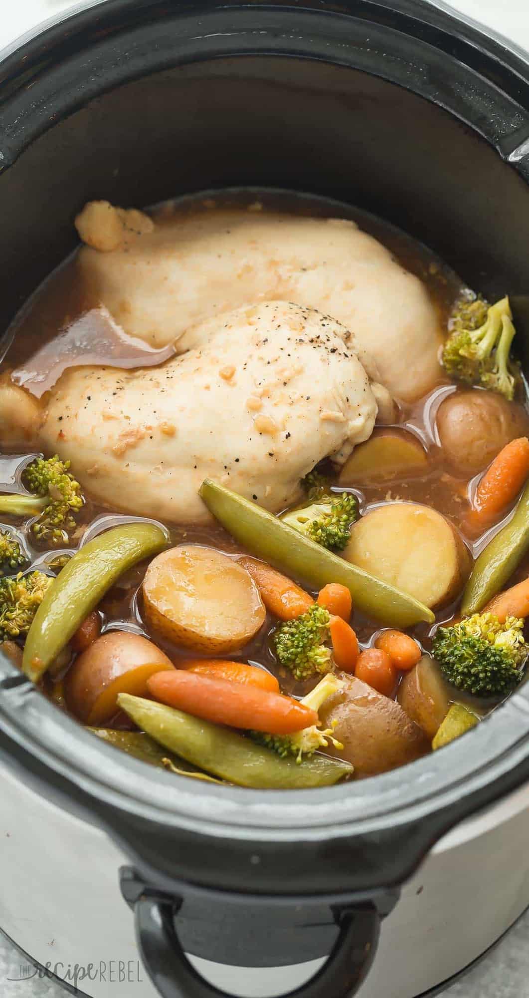 tall image of cooked chicken breast potatoes snap peas broccoli and carrots in black slow cooker