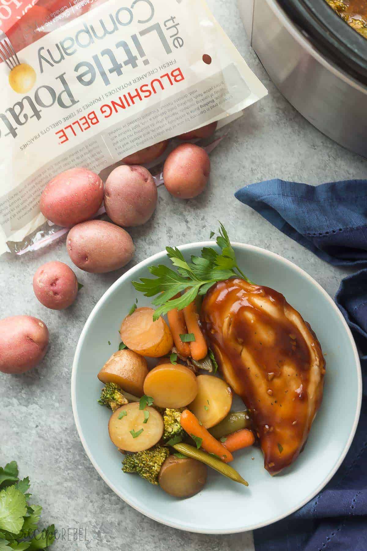 overhead image of honey garlic chicken and vegetables on a blue plate with an open bag of little potatoes