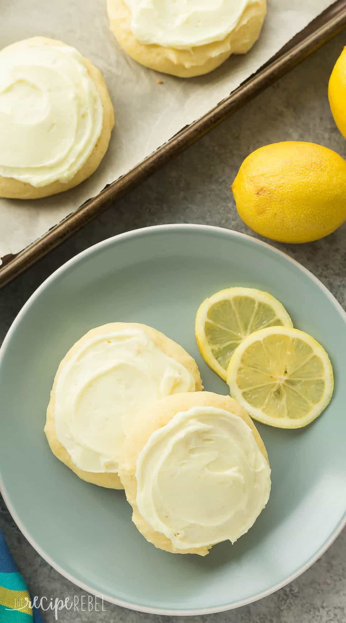 These Lemon Sour Cream Sugar Cookies are soft, moist and loaded with lemon! There's no chilling or rolling -- just stir, drop, bake and frost (if you want to!). Perfect for Easter or Christmas baking. Includes how to recipe video long image of lemon sour cream cookies overhead on blue plate with lemon slices