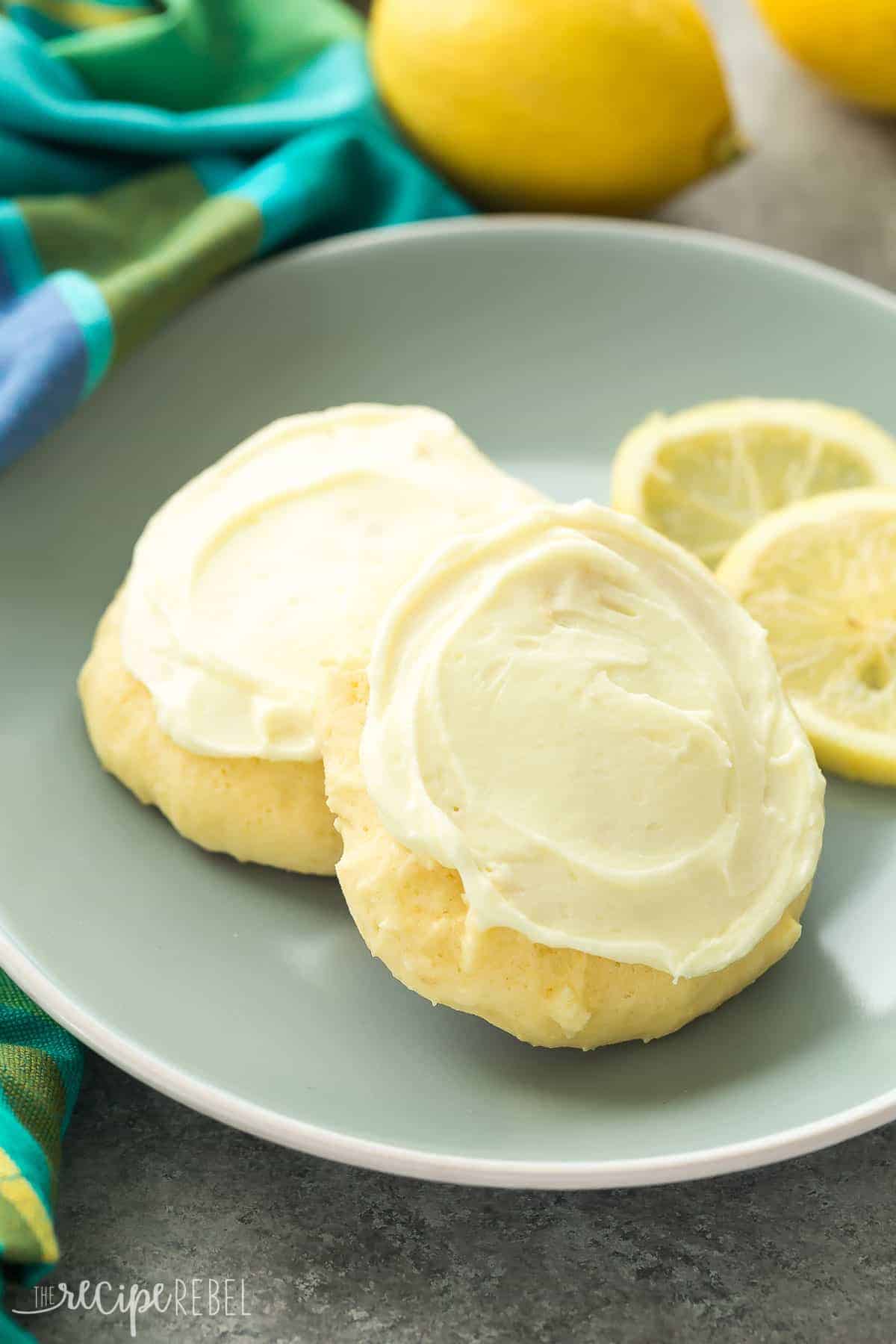 These Lemon Sour Cream Sugar Cookies are soft, moist and loaded with lemon! There's no chilling or rolling -- just stir, drop, bake and frost (if you want to!). Perfect for Easter or Christmas baking. Includes how to recipe video close up of lemon sour cream cookies with lemon frosting on blue plate