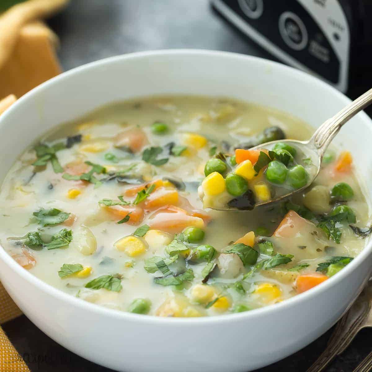 square image of bowl of creamy vegetable soup in front of slow cooker