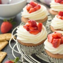 strawberry cheesecake cupcakes on white cooling rack with graham crackers and fresh strawberries on the side