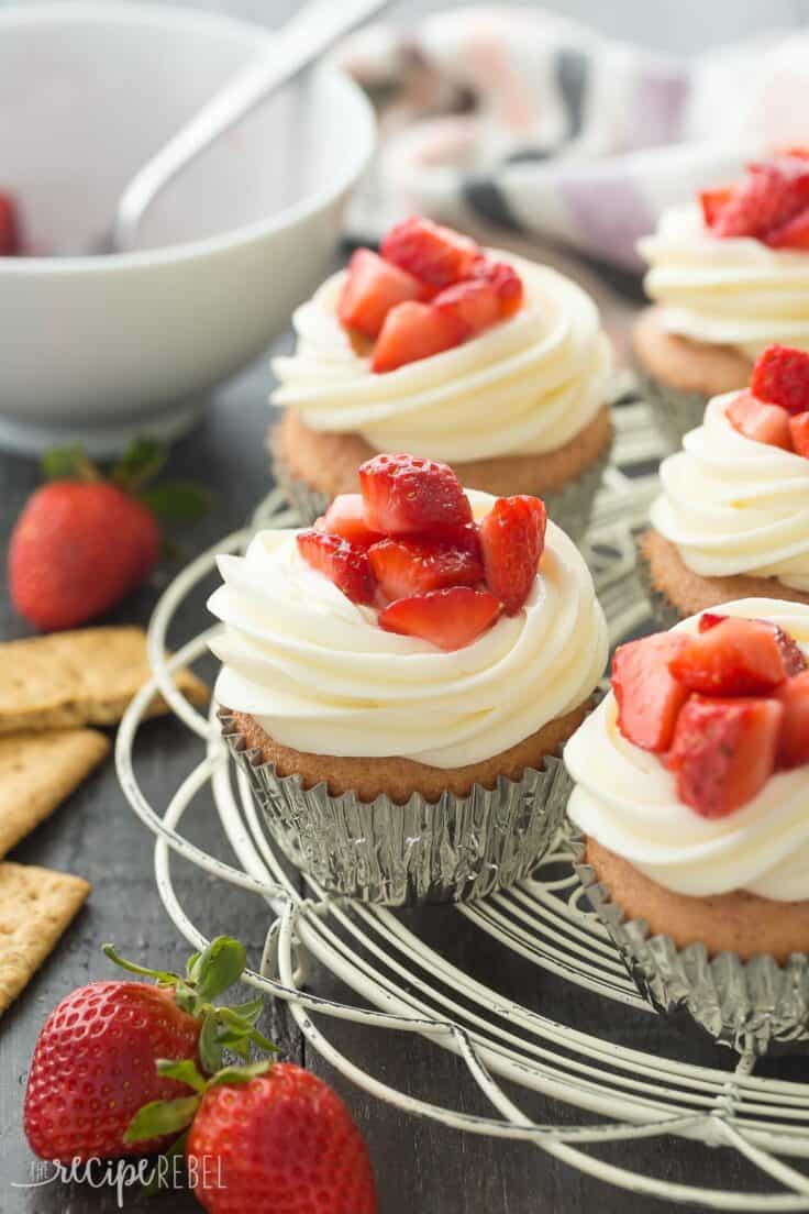 strawberry cheesecake cupcakes on white cooling rack with graham crackers and fresh strawberries on the side