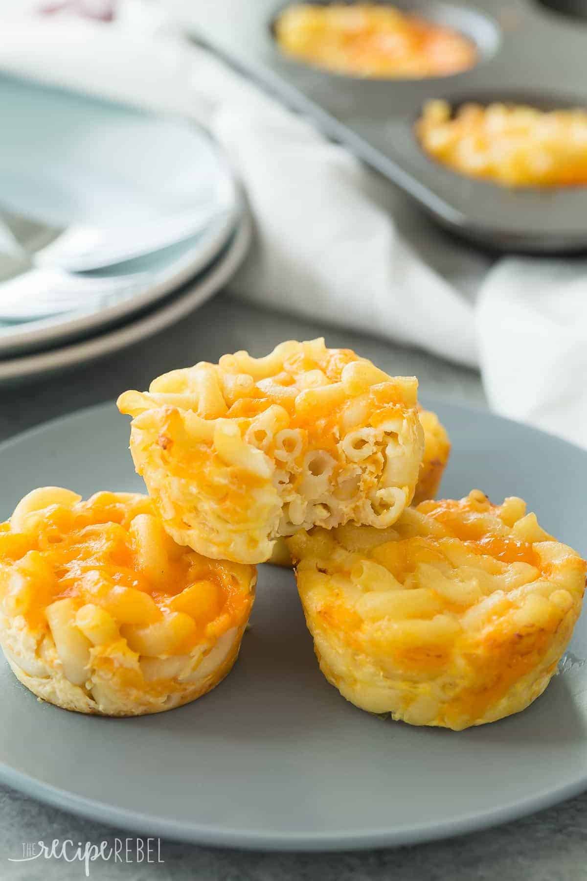 baked mac and cheese cups stacked on grey plate with one bite taken out of top cup