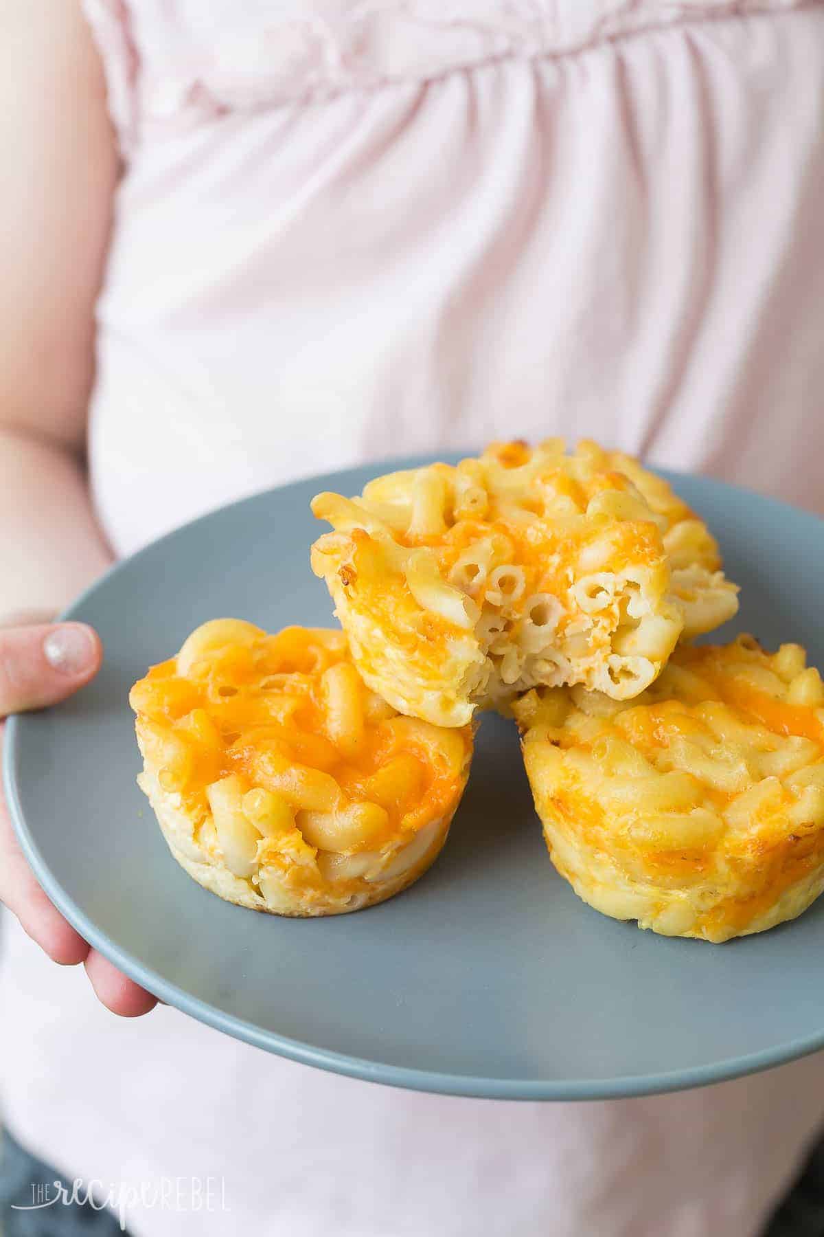 baked mac and cheese cups on grey plate held in child's hands