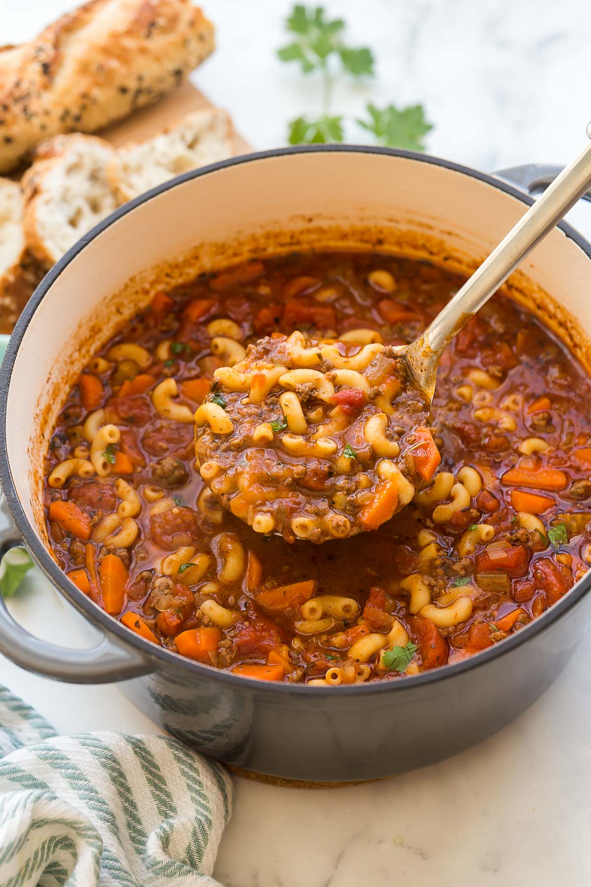 This Tomato Macaroni Soup is a hearty and healthy one-pot meal that’s ready in under 30 minutes. It’s packed with tender ground beef, whole wheat macaroni pasta, veggies, tomato sauce, and more! #soup #recipes #dinner | easy dinner ideas | healthy soup recipes | ground beef recipes | easy soup recipes metal ladle scooping beef and tomato macaroni soup