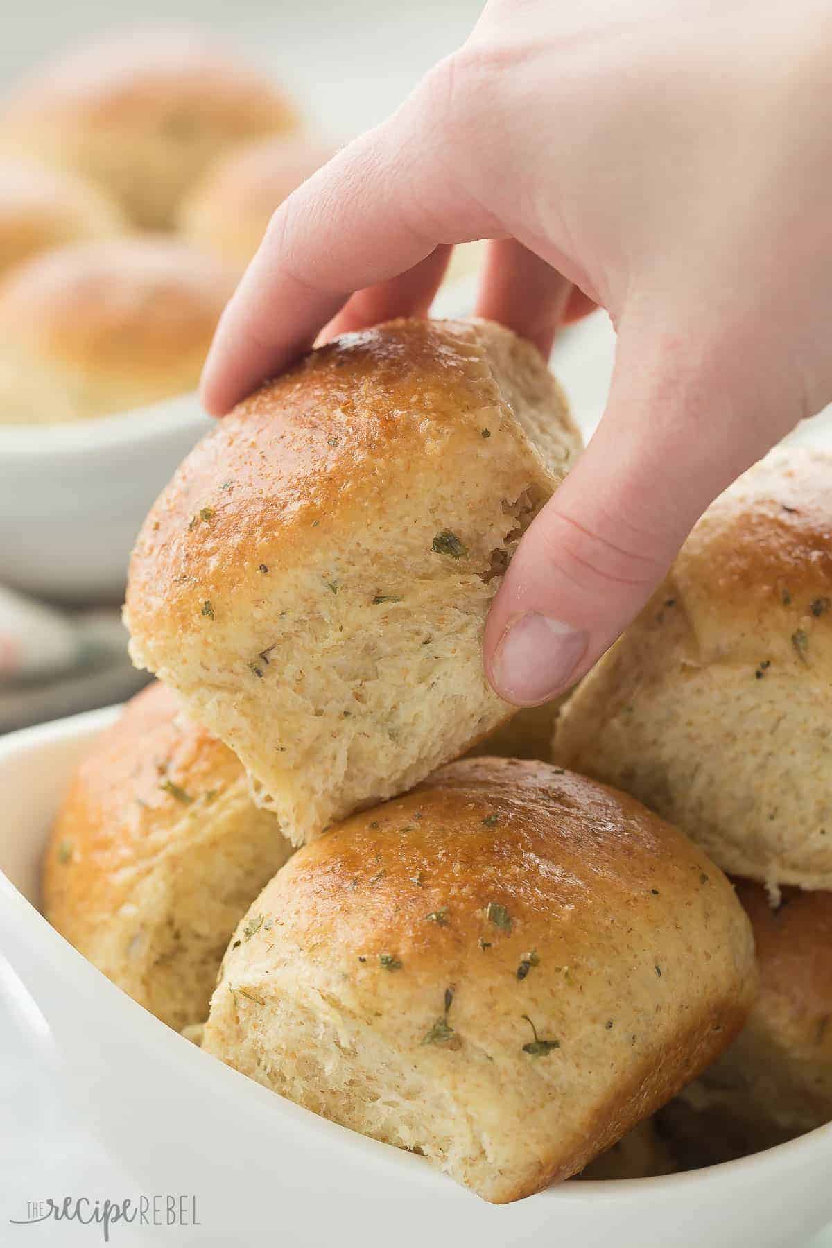 hand grabbing garlic herb dinner roll out of white bowl