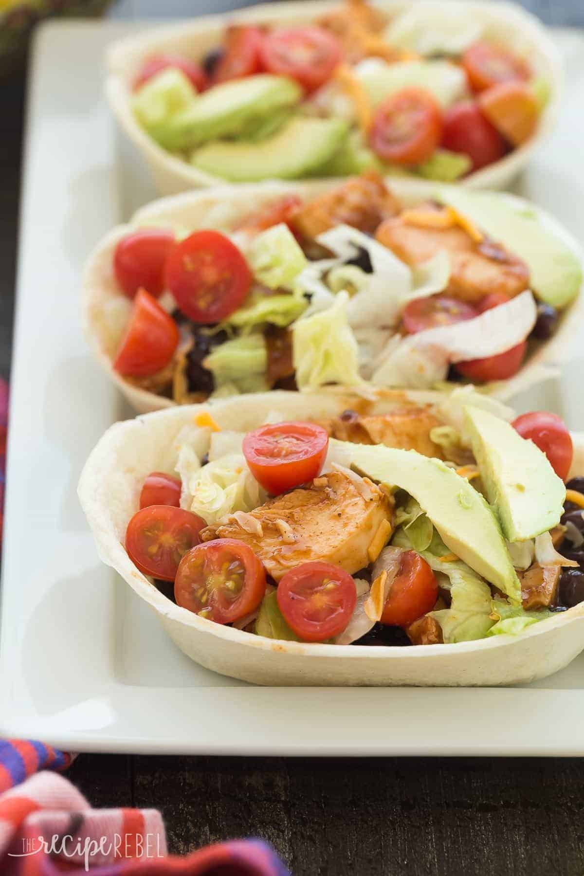 These BBQ Chicken Taco Bowls are an easy make ahead meal -- freezer friendly and perfect for your week's meal prep! The chicken can be made on the stovetop, in the slow cooker or Instant Pot. Includes step by step recipe video. bbq chicken taco bowls in soft tortilla bowls topped with fresh tomato and avocado