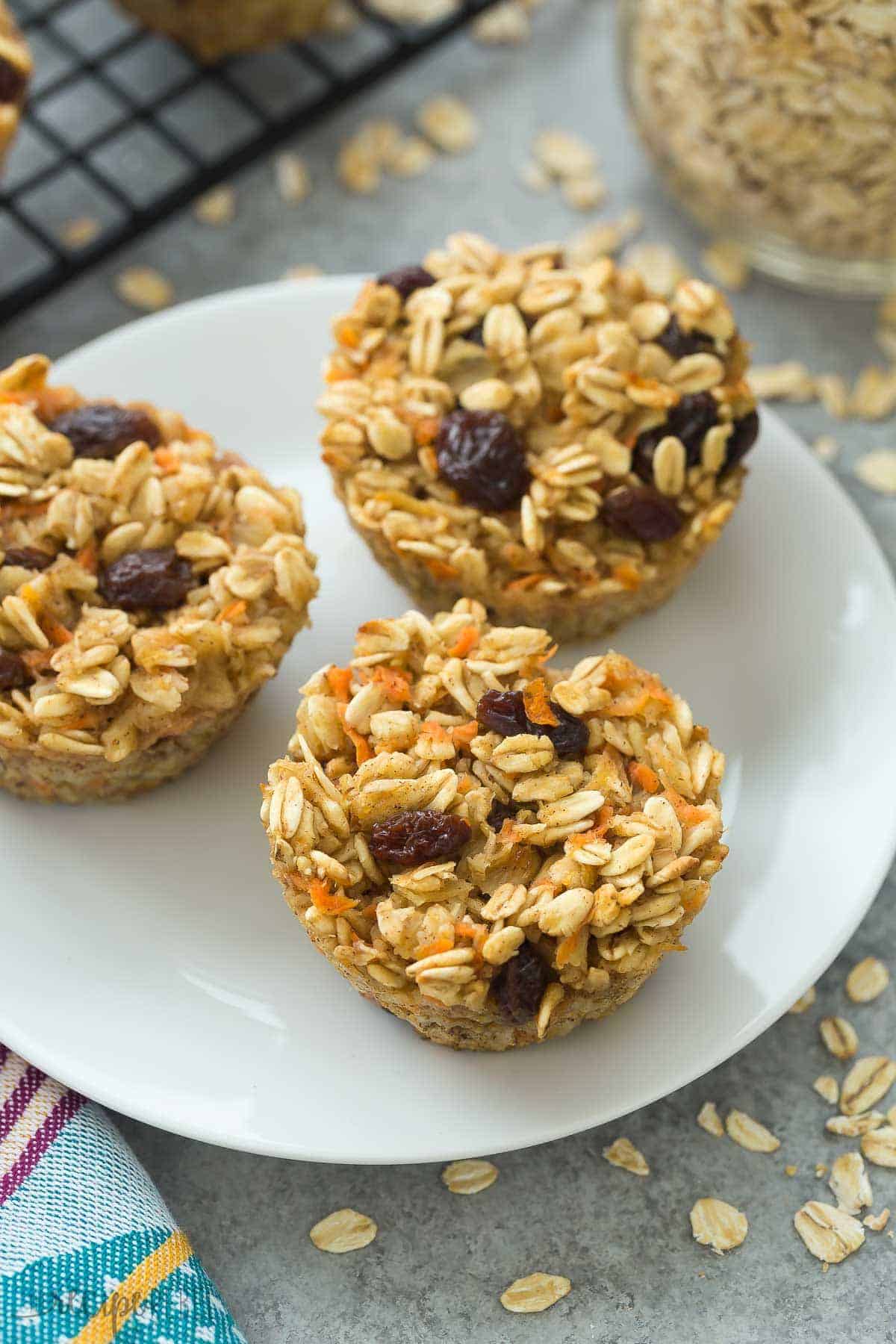 three baked oatmeal cups on a white plate close up with raw oats sprinkled around