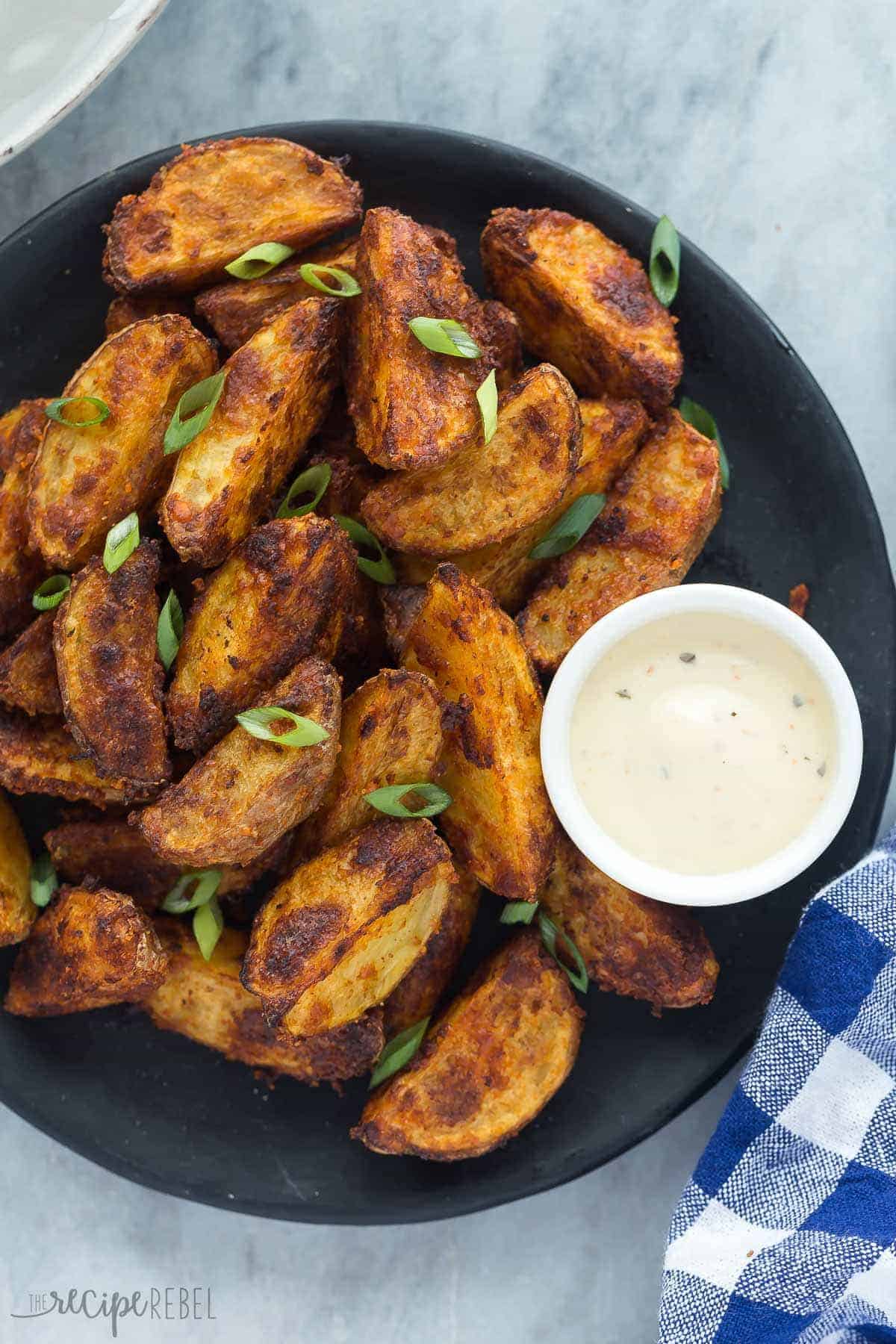 crispy potato wedges overhead on black plate with creamy sauce on the side and blue napkin