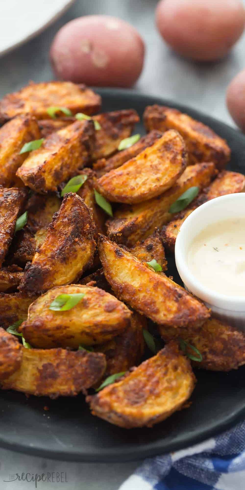 tall image of crispy chipotle parmesan potato wedges with creamy dipping sauce on plate