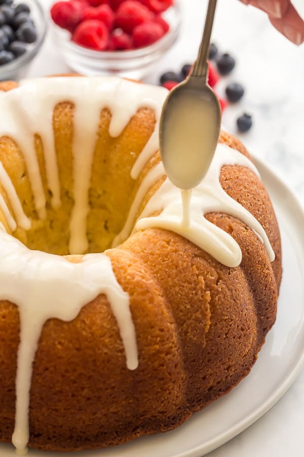 cream cheese glaze being drizzled over lemon bundt cake