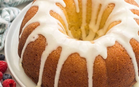 whole glazed lemon bundt cake with blueberries and raspberries in background
