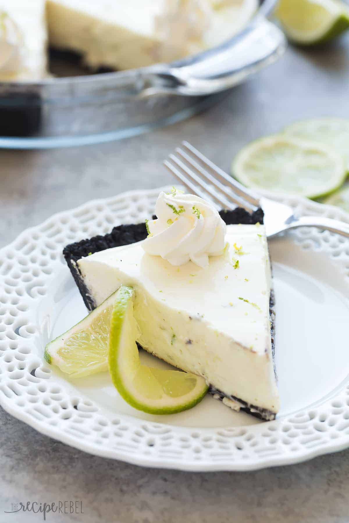 slice of key lime pie with chocolate crust on white plate with slice of lime