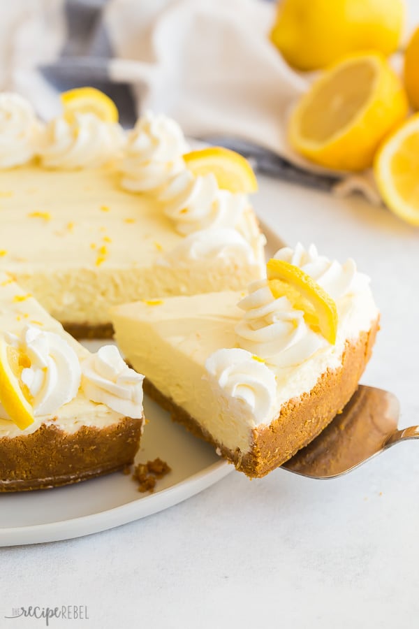 Fetta di cheesecake al limone al forno che viene tirata fuori con i limoni sullo sfondo