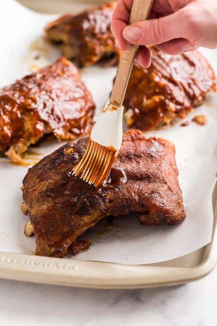 brushing cooked ribs with barbecue sauce on sheet pan