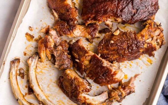 overhead image of meat falling off of bones of slow cooker ribs on sheet pan