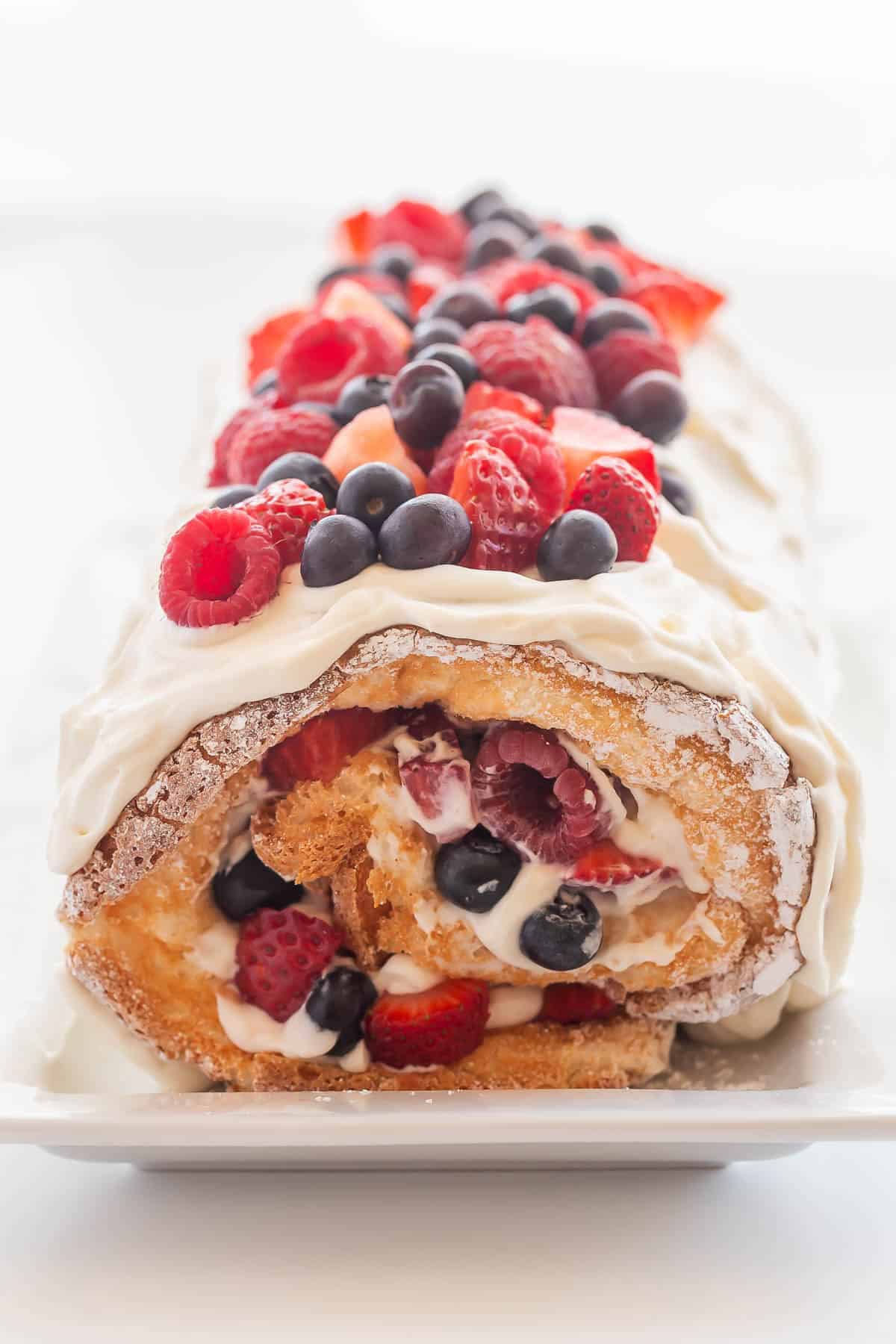 triple berry angel food cake roll with whipped cream cheese and berries on top.