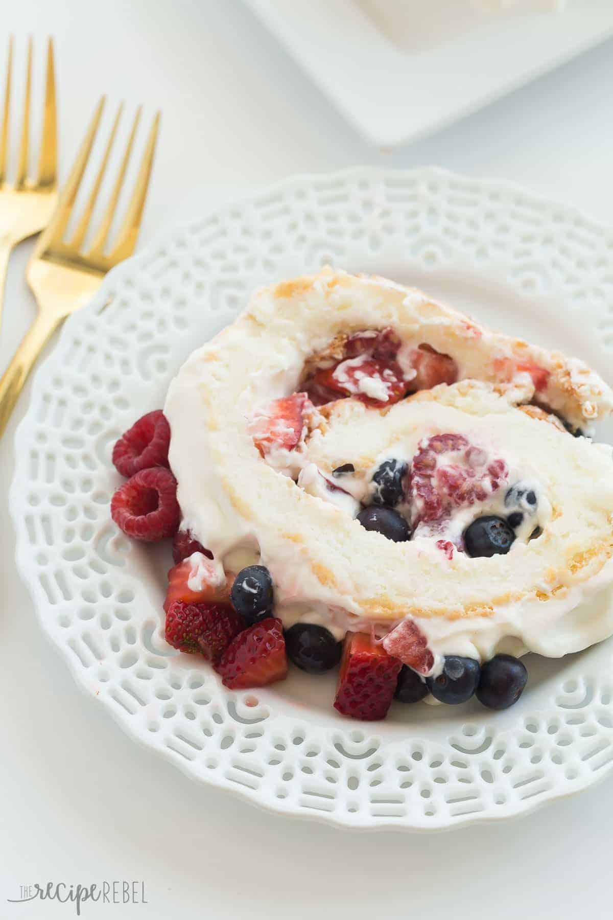 slice of triple berry angel food cake roll on white plate with gold fork on the side