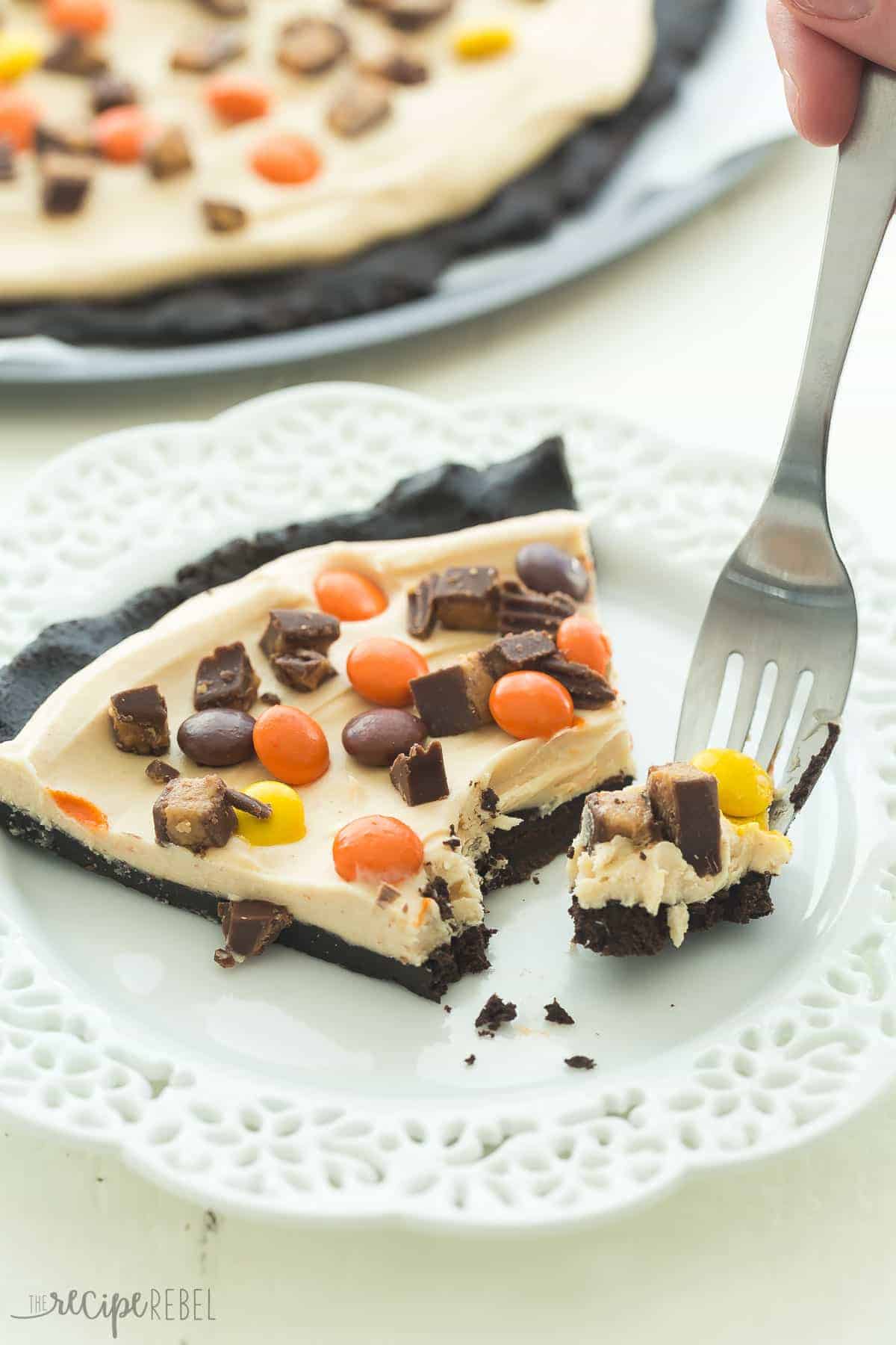 peanut butter cup dessert pizza piece on white plate with fork taking a bite